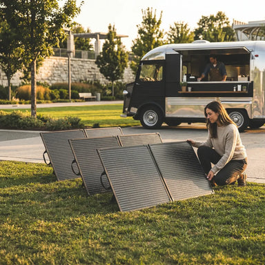 Multiple Lion Energy foldable solar panels set up on grass near a food truck for outdoor mobile solar power use