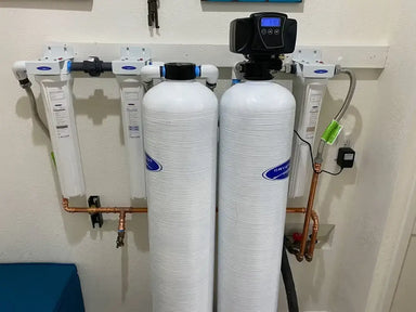 Installed Crystal Quest whole house water filtration system featuring white tanks and copper piping on a garage wall.
