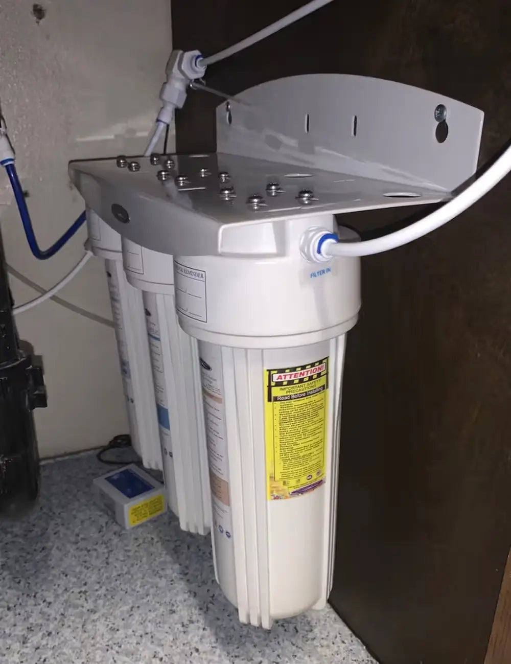 Crystal Quest SMART triple-stage under-sink water filtration system installed inside a kitchen cabinet with wall-mounted bracket and tubing.