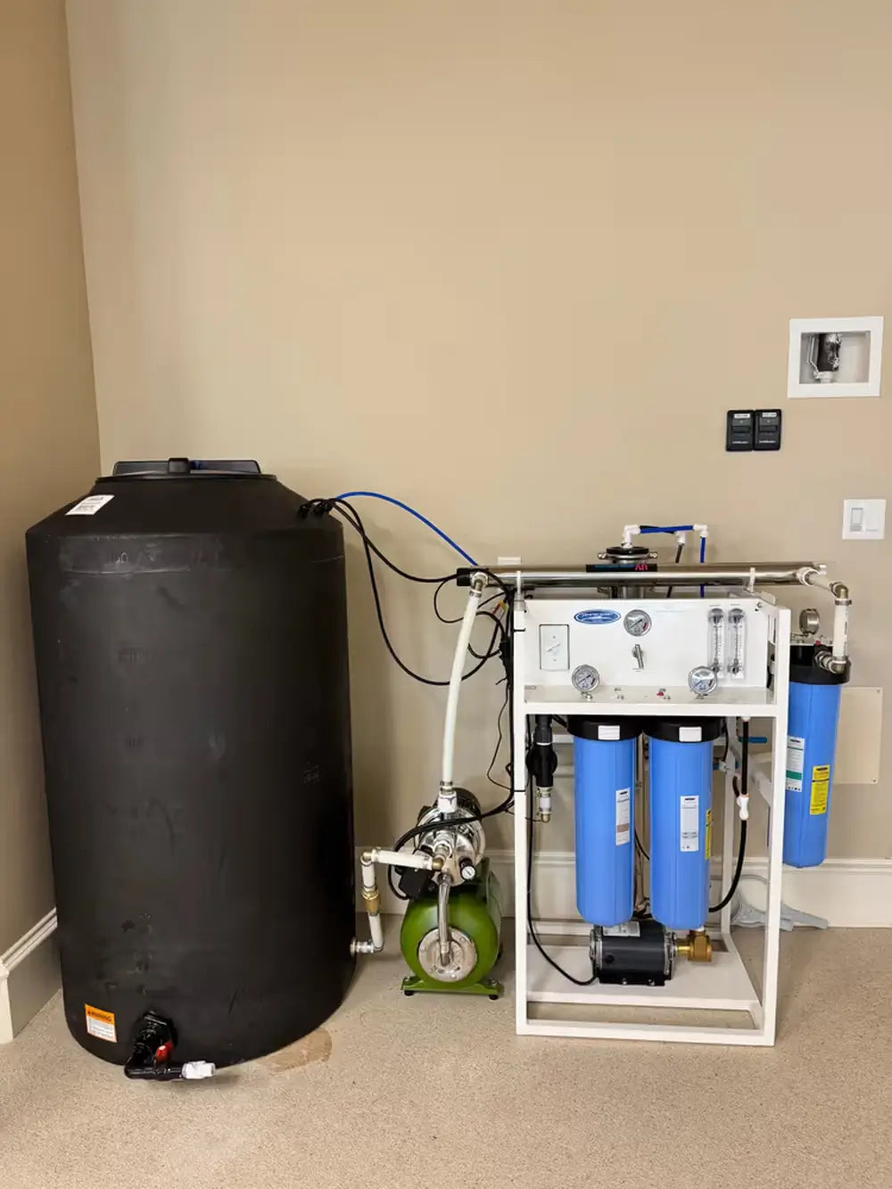 Complete Crystal Quest whole house RO installation including the filtration rack, a large black water storage tank, and a green delivery pump.