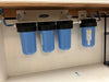 Real-life under-counter installation of a Crystal Quest multi-stage water filtration system with pressure gauges and PEX piping.