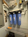 Triple Crystal Quest Big Blue SMART whole house water filter wall-mounted in a utility closet with pressure gauges.