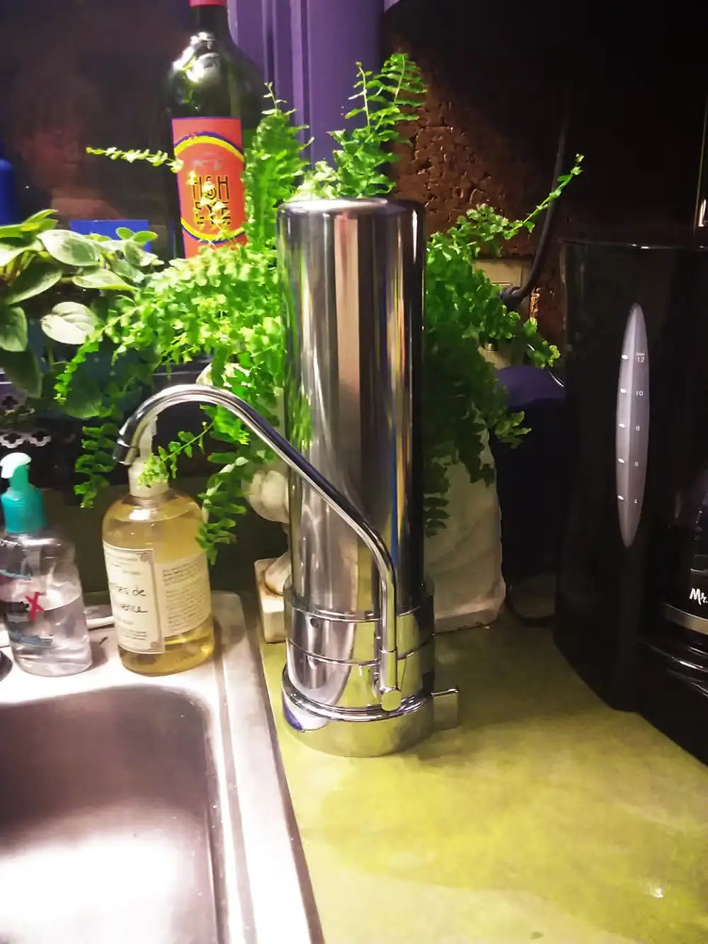 Crystal Quest stainless steel SMART countertop water filter system for arsenic removal installed next to a kitchen sink.