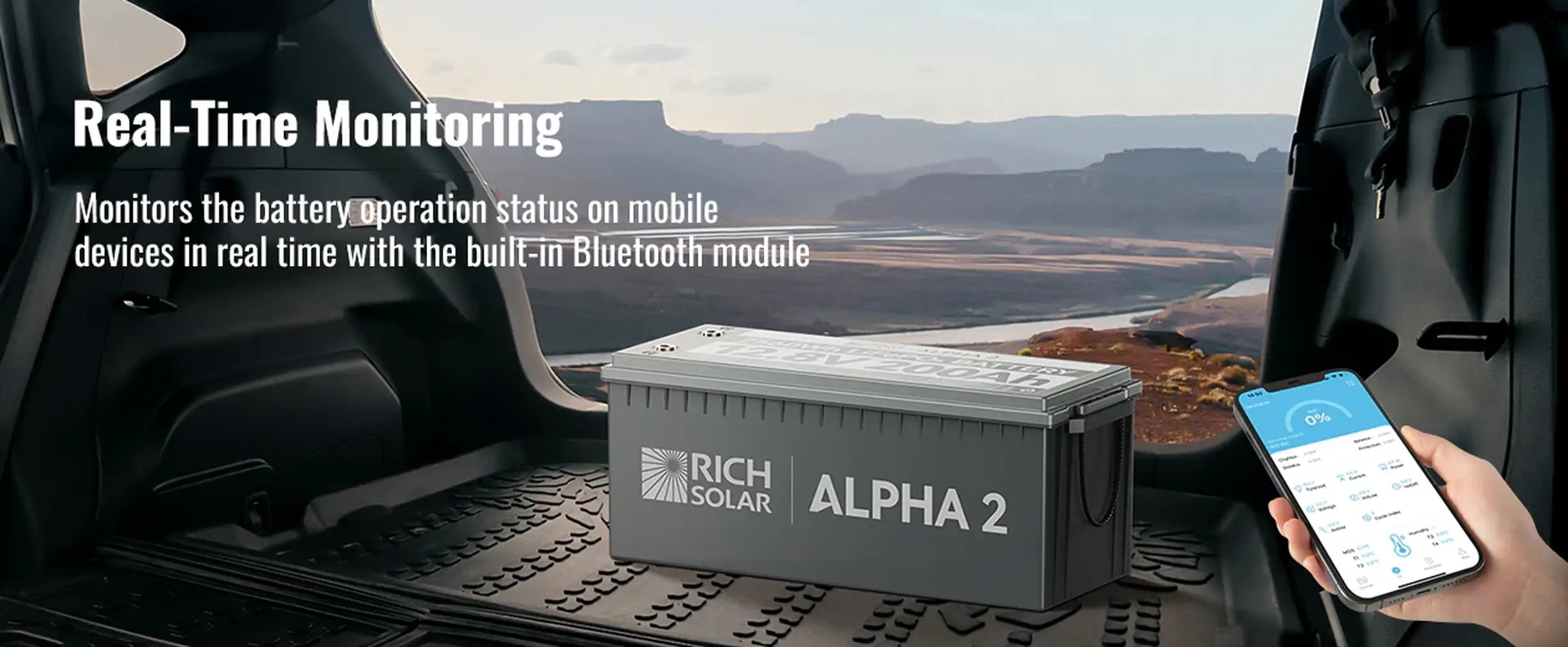 Rich Solar Alpha 2 12V lithium battery installed in an SUV trunk overlooking a canyon, with a hand holding a smartphone demonstrating real-time Bluetooth app monitoring.