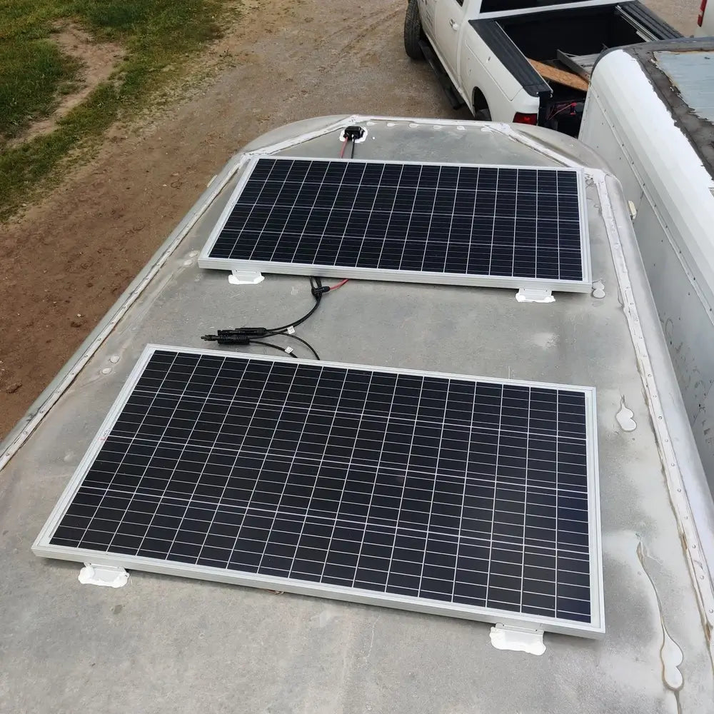 Off-grid RV solar panel installation featuring two rigid panels mounted securely with brackets on a curved aluminum camper trailer roof.