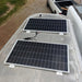 Off-grid RV solar panel installation featuring two rigid panels mounted securely with brackets on a curved aluminum camper trailer roof.