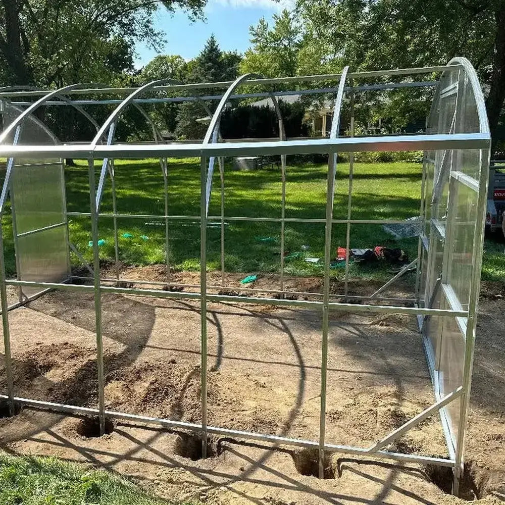 Assembly phase of the GreenhouseToGrow Magnolia 10x6.5 Greenhouse showing the steel frame structure set over base post holes for anchoring.