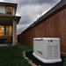 Installed Generac 10kW home standby generator beside house and wooden fence under stormy sky