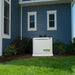 Front view of Generac 10kW standby generator installed beside blue house with landscaped garden