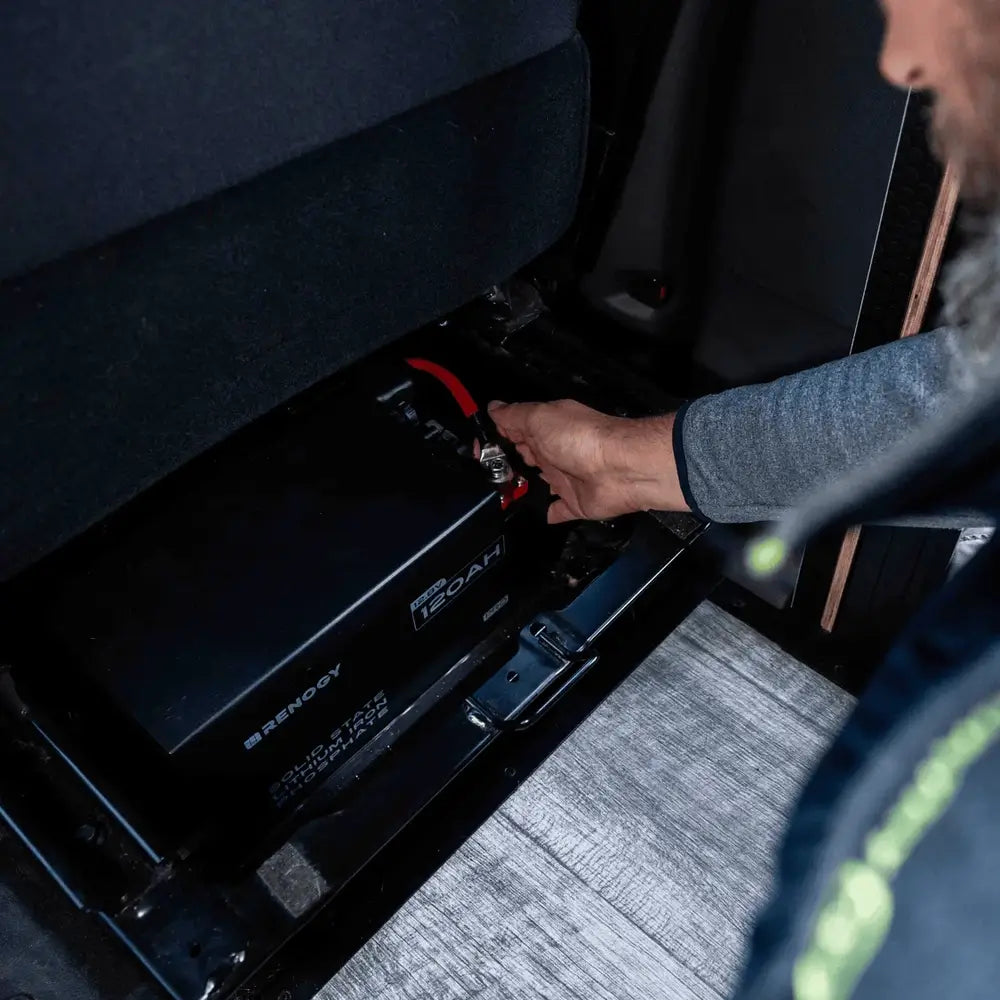 Compact installation of a Renogy Pro S1 12V 120Ah lithium battery into a tight compartment underneath an RV passenger seat.