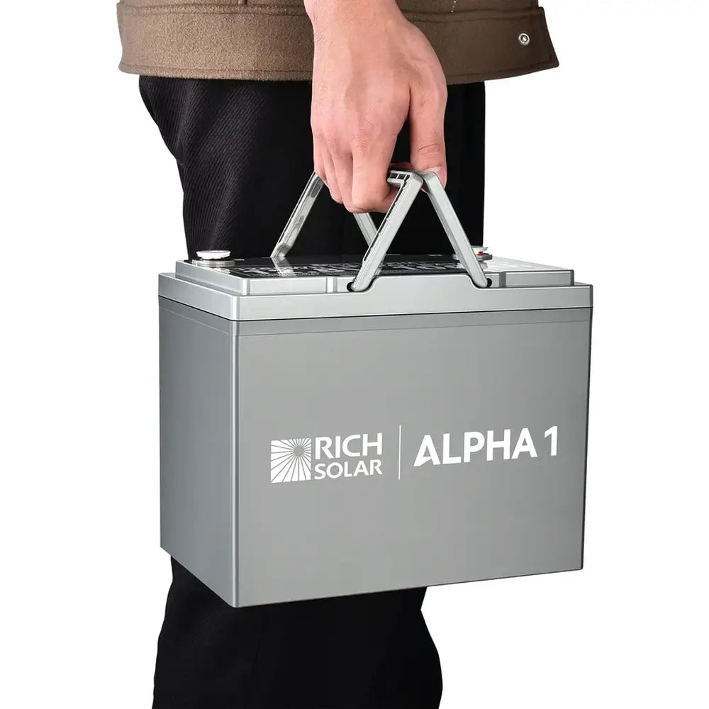 Side view of a person easily carrying the portable Rich Solar ALPHA 1 12V lithium battery using its built-in handles.