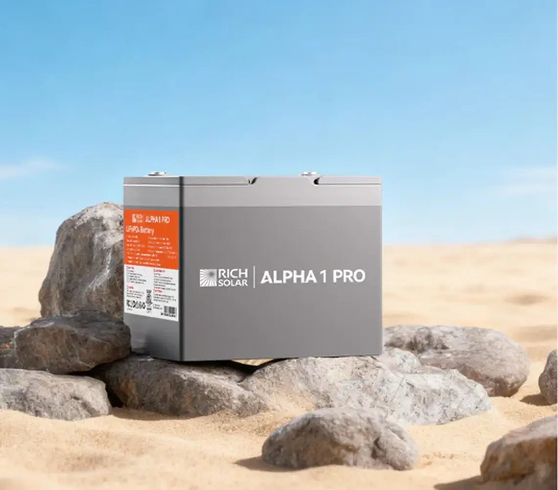 Rich Solar ALPHA 1 PRO 12V 100Ah LiFePO4 battery sitting on desert rocks under a clear blue sky, showcasing its outdoor and off-grid durability.