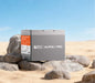 Rich Solar ALPHA 1 PRO 12V 100Ah LiFePO4 battery sitting on desert rocks under a clear blue sky, showcasing its outdoor and off-grid durability.