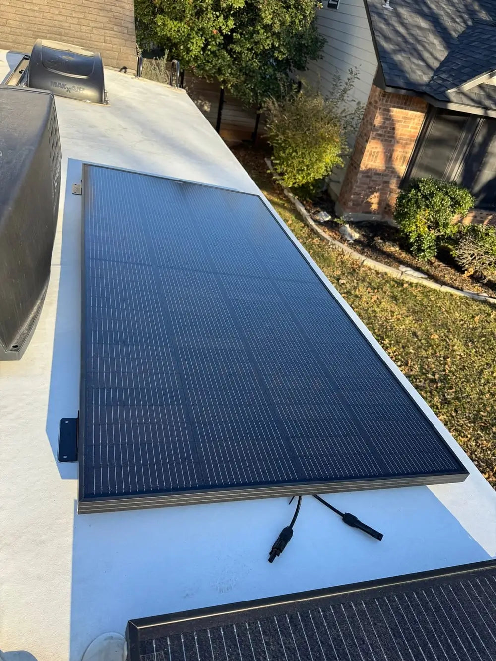 Close-up of an all-black Rich Solar 250W monocrystalline solar panel mounted flat on a white RV roof with disconnected MC4 cables.