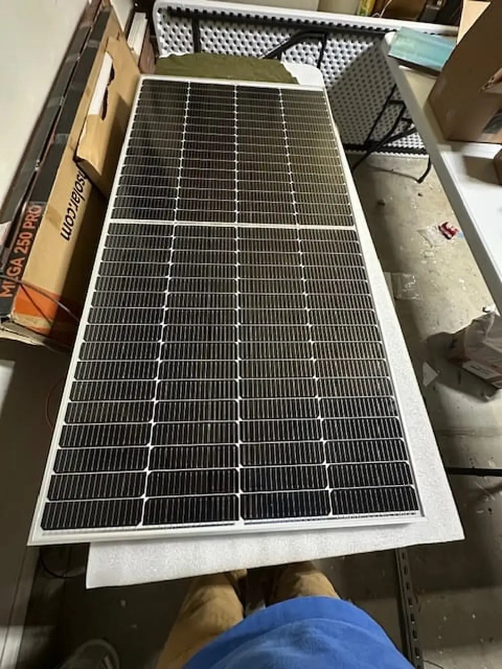 Rich Solar MEGA 250 PRO 24V monocrystalline solar panel with silver frame lying flat on a workbench next to its original cardboard packaging.