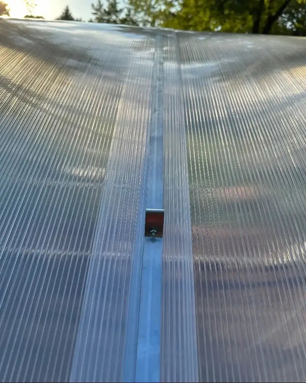 Close-up of the metal fastening clip and overlapping polycarbonate panels on the roof of a GreenhouseToGrow Magnolia kit.