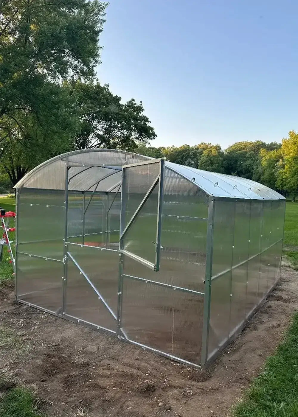 Side profile of a 32.5-foot long GreenhouseToGrow Magnolia polycarbonate greenhouse kit fully assembled on a prepared dirt base.