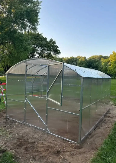 Side profile of a 32.5-foot long GreenhouseToGrow Magnolia polycarbonate greenhouse kit fully assembled on a prepared dirt base.