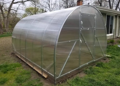 A fully assembled GreenhouseToGrow Camellia 10x6.5 Greenhouse Kit featuring a heavy-duty galvanized steel arched frame and clear polycarbonate panels installed in a residential backyard.
