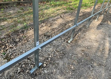 Close-up detail of the GreenhouseToGrow Camellia 10x6.5 Greenhouse Kit’s galvanized steel base and vertical frame supports being anchored into the ground for maximum stability.