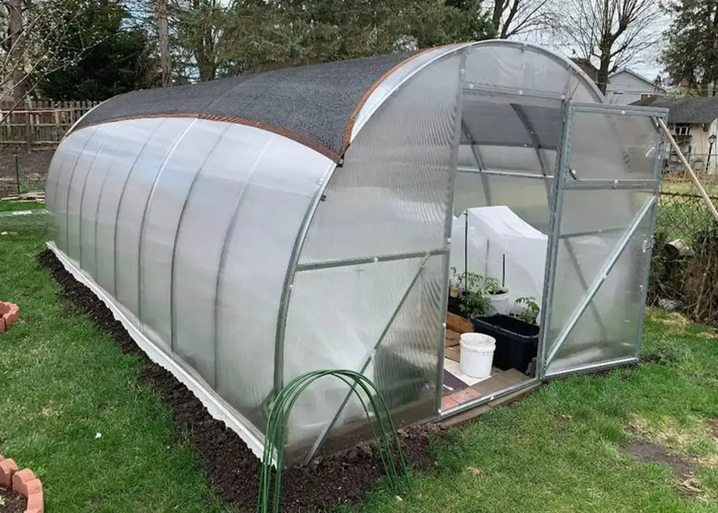Exterior side view of the GreenhouseToGrow Camellia 10x13 Greenhouse Kit installed in a backyard with a black sun shade cloth for temperature control.