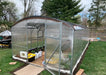 Interior view of a Magnolia Greenhouse showing active plant cultivation, interior bracing, and a protective shade cloth installed over the curved polycarbonate roof.