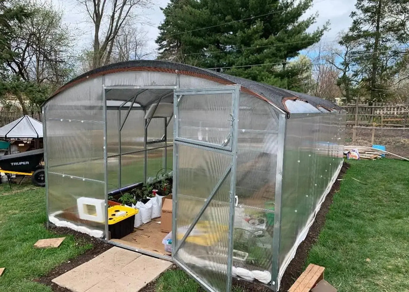 Interior view of a Magnolia Greenhouse showing active plant cultivation, interior bracing, and a protective shade cloth installed over the curved polycarbonate roof.