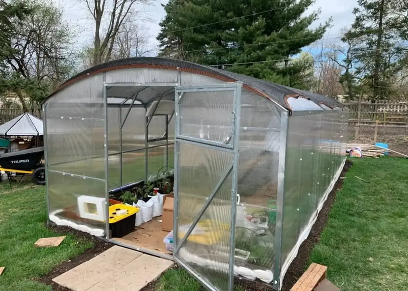 Fully assembled GreenhouseToGrow Magnolia 10x32.5 Greenhouse Kit featuring a black roof shade cloth and interior garden plants.