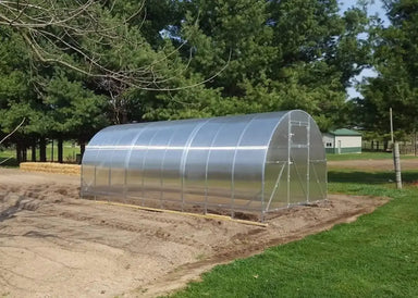 A fully assembled GreenhouseToGrow Camellia 10x39 Greenhouse Kit standing in an open field, showcasing its spacious tunnel design and translucent panels.