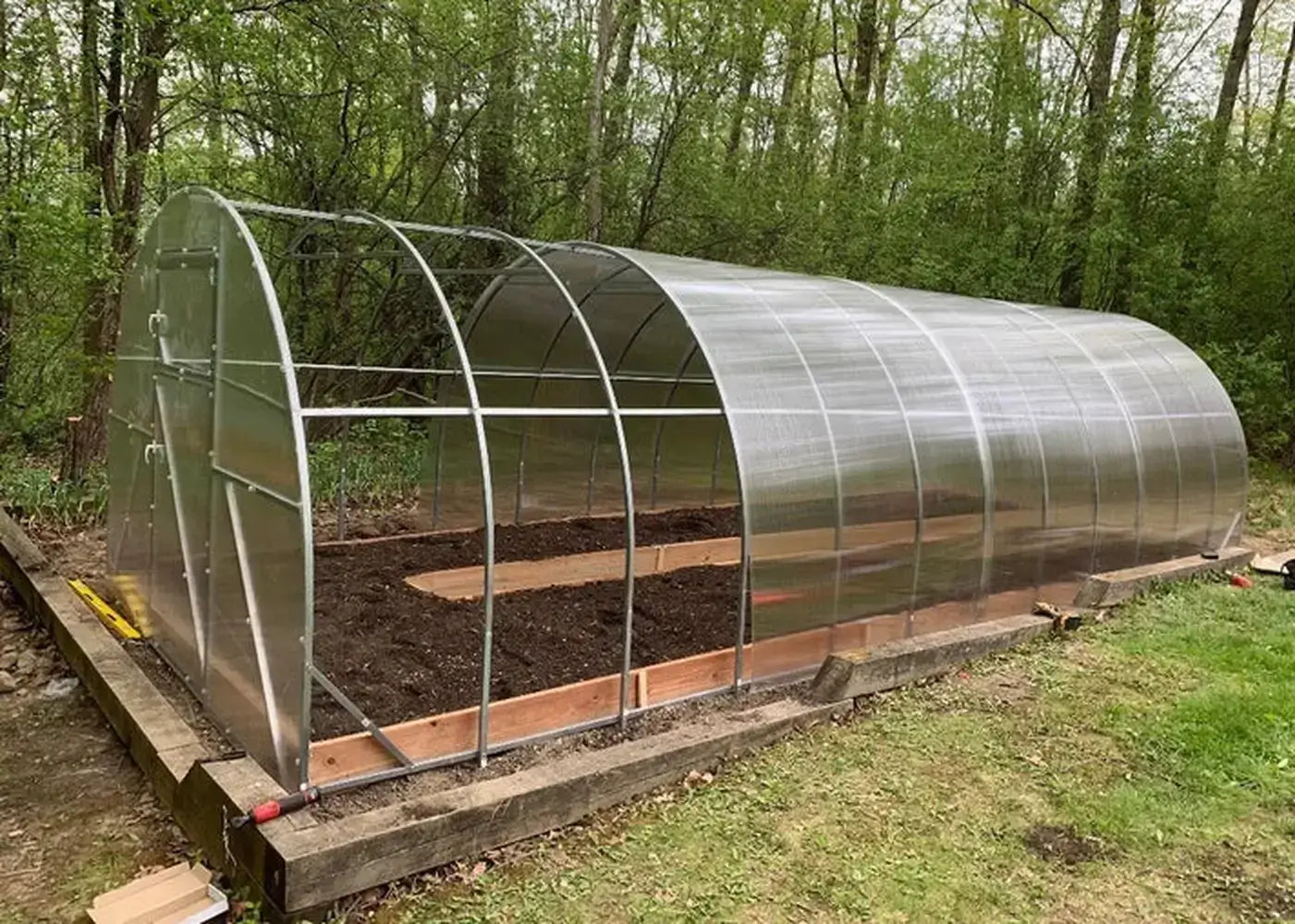Mid-assembly view of the GreenhouseToGrow Camellia 10x13 Greenhouse Kit with polycarbonate panels partially installed over the arched frame.