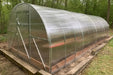 Angled exterior view of the GreenhouseToGrow Camellia 10x39 Greenhouse Kit installed in a wooded backyard setting with a level timber base.