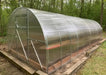 Perspective view of the GreenhouseToGrow Camellia 10x13 Greenhouse Kit showing the sleek, rust-resistant galvanized steel structure against a wooded backdrop.