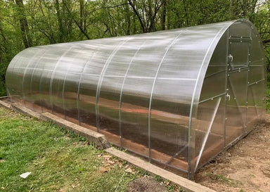 Side view of the finished GreenhouseToGrow Camellia 10x26 greenhouse kit nestled in a wooded backyard setting.