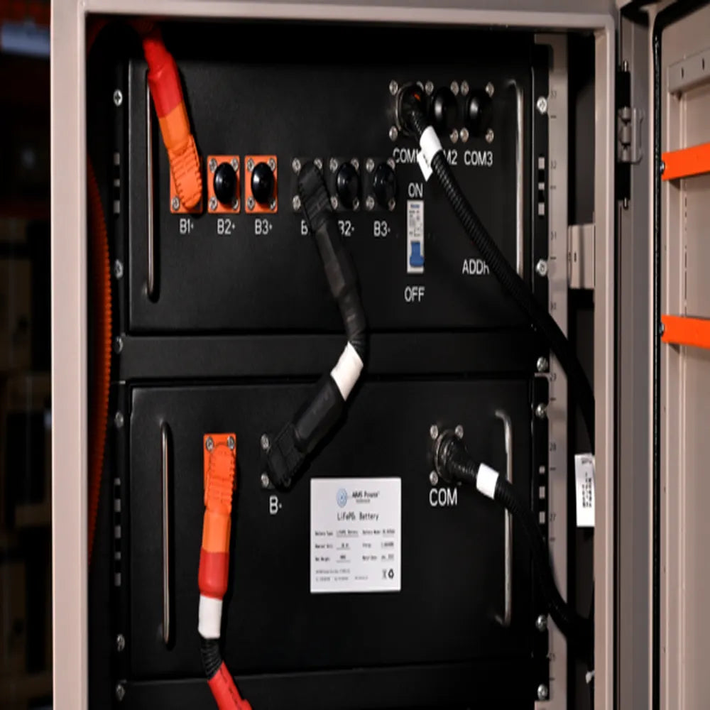 Close-up of AIMS Power LiFePO4 battery module ports, B terminals, COM connections, on/off switch, and orange power cables.