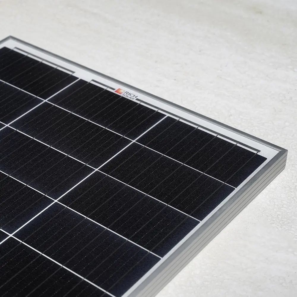 Corner perspective shot of a Rich Solar MEGA 100W 12V solar panel resting on a light-colored smooth surface.