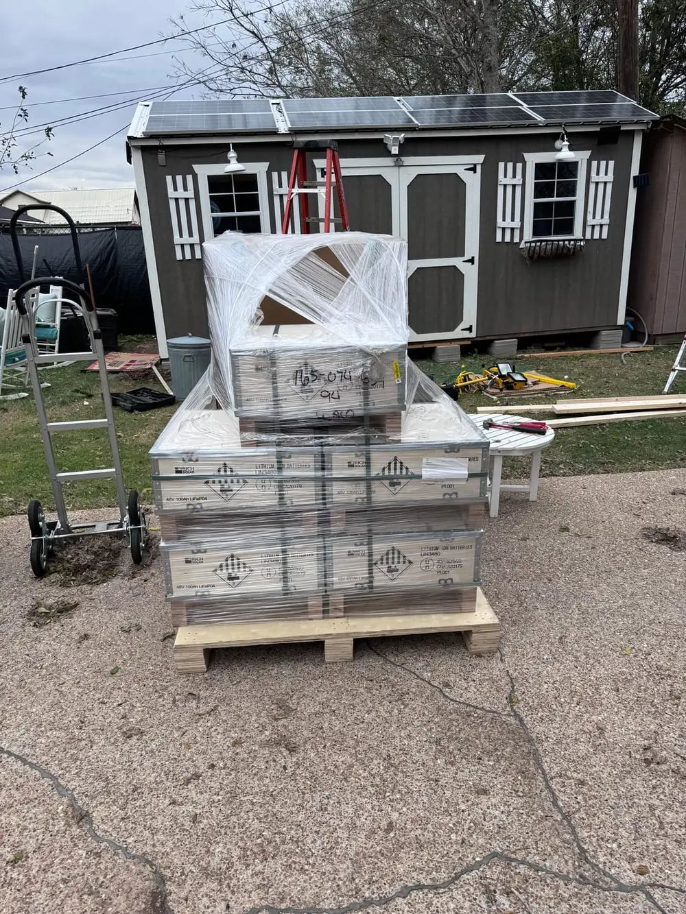 Freight shipment of Rich Solar 48V 100Ah LiFePO4 lithium-ion batteries with visible class 9 hazard labels delivered in front of a solar shed.