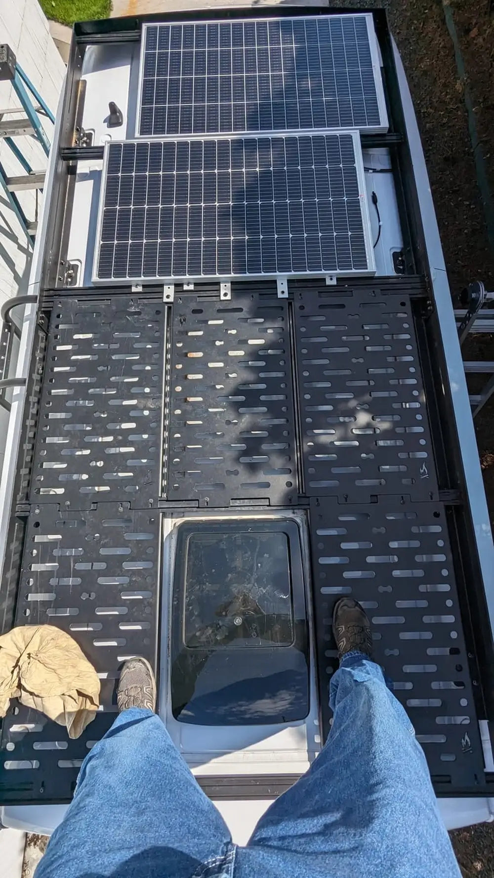 Two off-grid solar panels installed on an adjustable dual pole mount system next to a rustic woodland cabin.