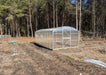 Wide-angle view of a completed GreenhouseToGrow Magnolia 10x32.5 Greenhouse Kit in a large backyard with a forest backdrop.