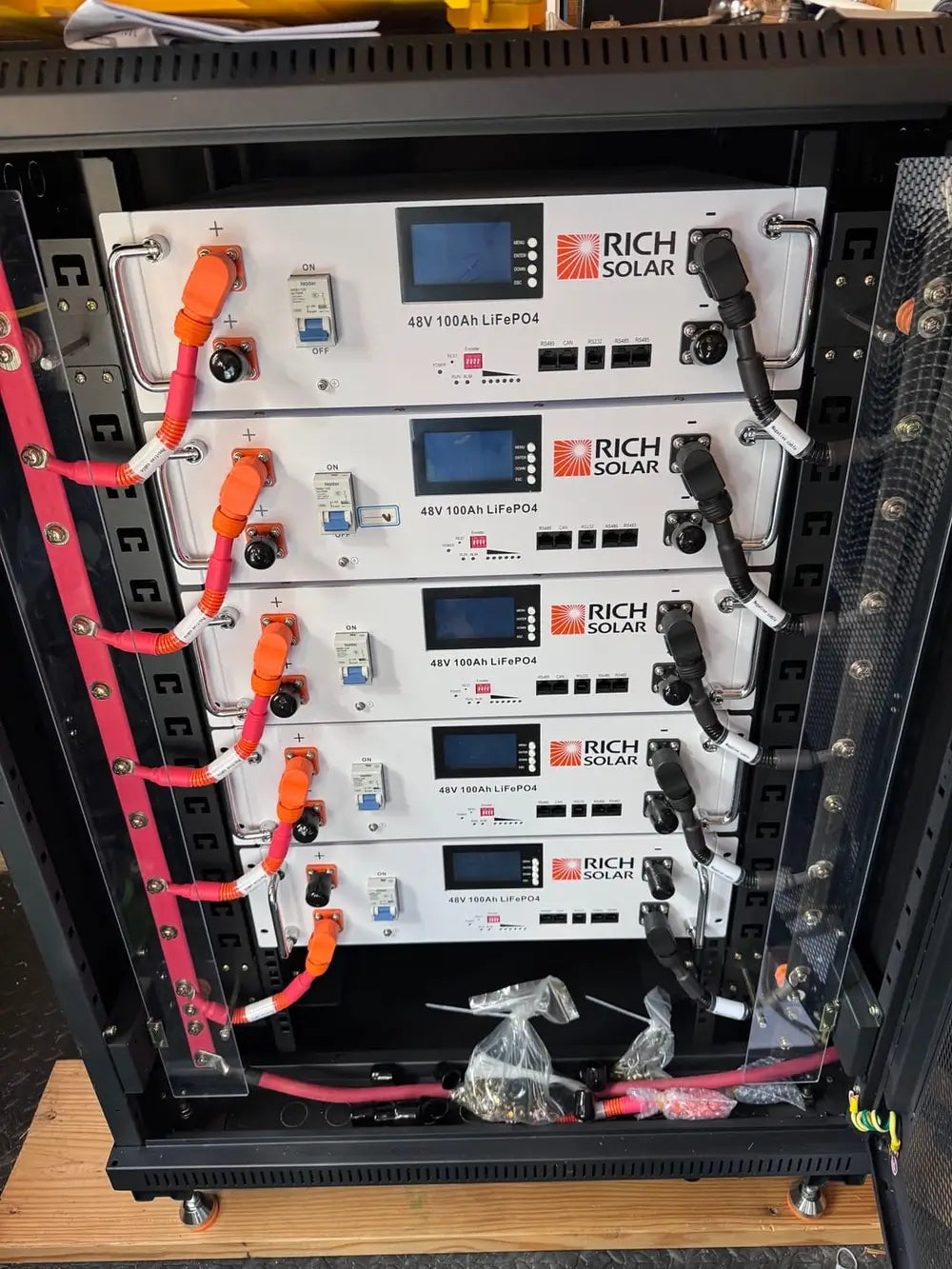 Interior view of five Rich Solar ALPHA 5 48V 100Ah solar server rack batteries wired in parallel with heavy-duty red and black power cables.