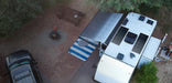 Aerial view of two Rich Solar MEGA 200 PRO 24V solar panels mounted flat on an RV camper roof at a wooded campsite.