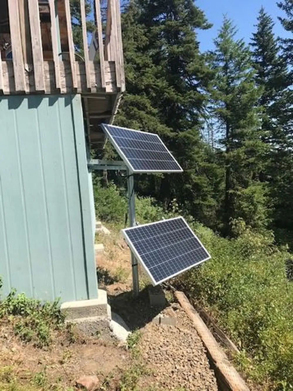 Overhead view of a DIY camper van solar setup showing two rigid panels integrated onto a black modular roof rack platform deck.