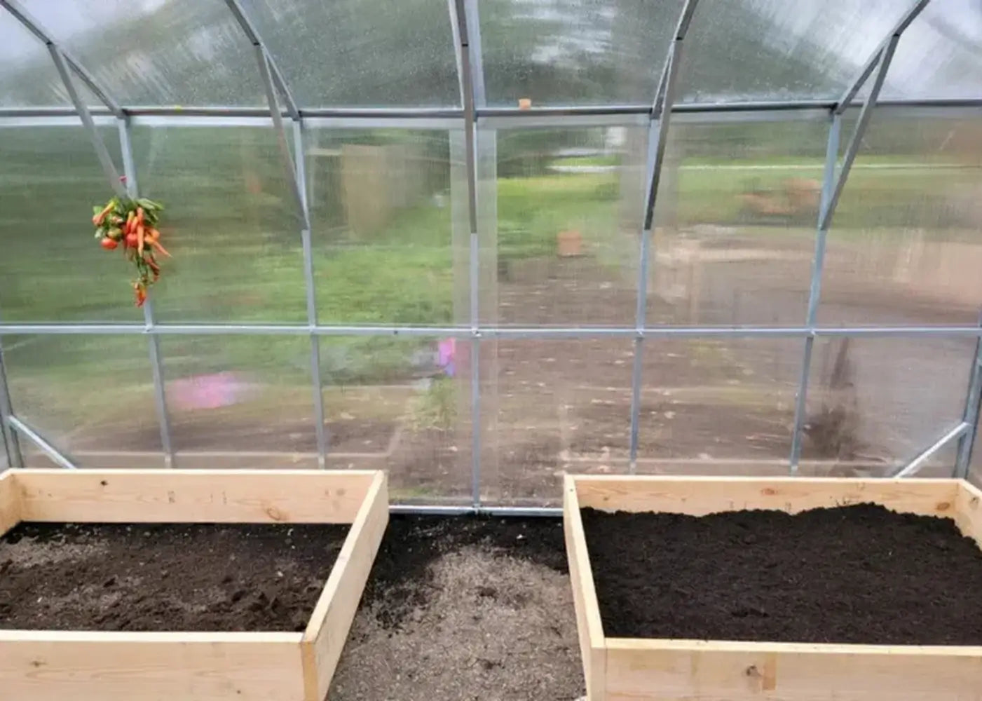 Inside the Magnolia 10x13 Greenhouse Kit showing empty wooden raised garden beds and the clear view through the polycarbonate walls.