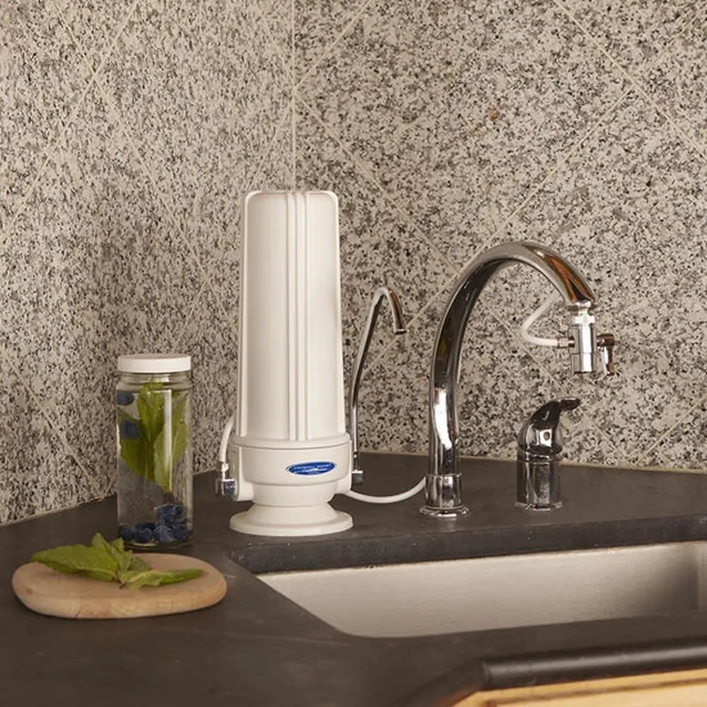 White Crystal Quest Nitrate SMART Countertop Water Filter System installed on a granite kitchen counter next to a faucet for clean drinking water.