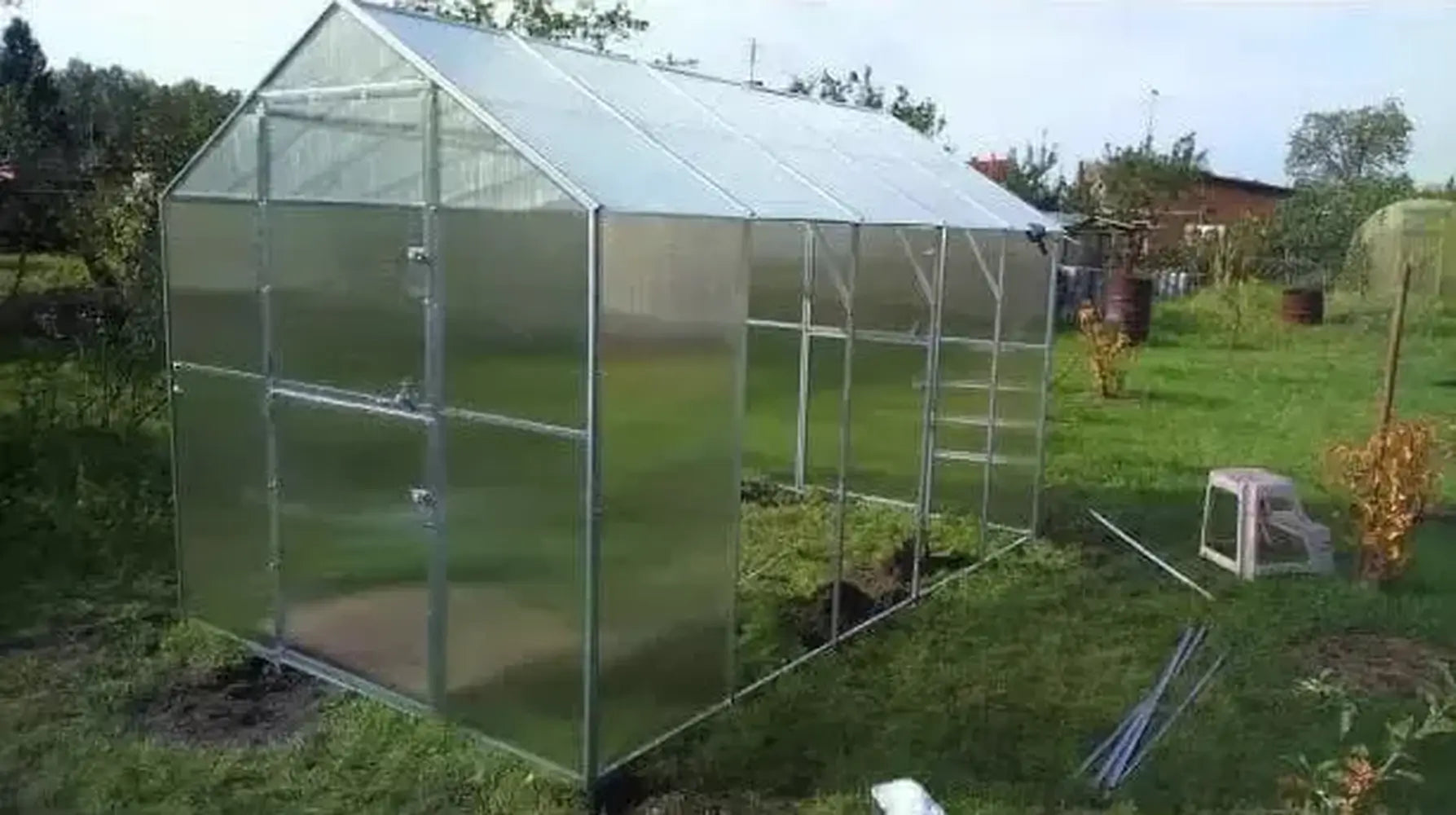 Mid-assembly view of the Daisy Greenhouse Kit showing the installation of polycarbonate side panels onto the metal frame.