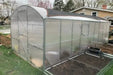 Side view of the GreenhouseToGrow Magnolia kit with an integrated roof shade cloth and a metal raised garden bed positioned in the foreground for a complete gardening setup.
