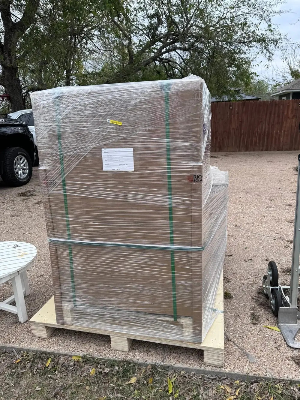 Side profile view of a large freight pallet containing a shrink-wrapped Rich Solar server rack cabinet box during residential delivery.
